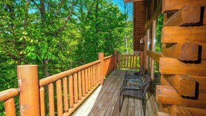 A wooden deck with a railing, chairs, and a view of dense green trees. - Great location with hot tub and pool table! Cute and classy log cabin! (Sevierville)