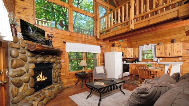 A cozy cabin interior with a stone fireplace, wooden walls, a dining area, and a kitchen. - Great location with hot tub and pool table! Cute and classy log cabin! (Sevierville)