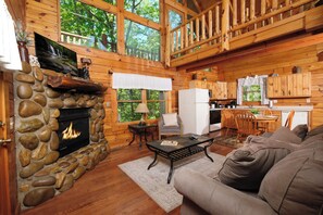 A cozy cabin interior with a stone fireplace, wooden walls, a dining area, and a kitchen. - Great location with hot tub and pool table! Cute and classy log cabin! (Sevierville)