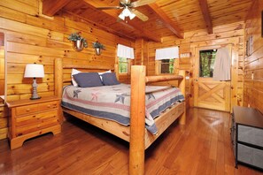 Un dormitorio de cabaña de madera con cama, mesita de noche, lámpara y cómoda.