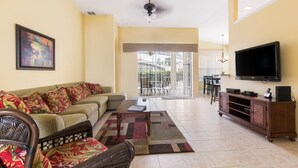 A living room with a sofa, a coffee table, a TV, and a dining area with chairs and a table. - Modern Villa w/ South-Facing Pool, Spa & Game Room Near Disney (Kissimmee)
