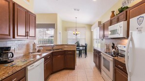 A kitchen with brown cabinets, a dishwasher, a microwave, and a refrigerator. - Modern Villa w/ South-Facing Pool, Spa & Game Room Near Disney (Kissimmee)
