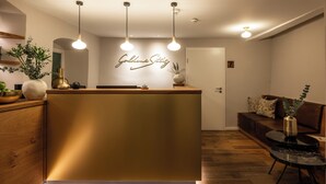 A reception area with a gold counter, pendant lighting, a wall sign, a wooden floor, and a brown sofa. - Hotel Goldene Steig (Kempten)