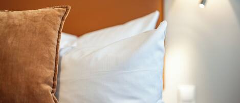 Una cama con dos almohadas, una marrón y otra blanca, y una lámpara de noche.