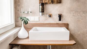 A bathroom with a wooden vanity, a white sink, a mirror with a wooden frame, a tissue dispenser, and a trash can.