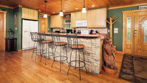 Une cuisine avec des meubles de rangement en bois, un îlot central doté de tabourets, un réfrigérateur, un four à micro-ondes et une sculpture d’ours en bois.