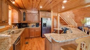 A spacious kitchen with wooden cabinets, granite countertops, stainless steel appliances, and a built-in island with bar stools.