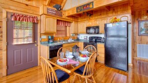 Una cocina tipo cabaña de madera con una mesa de comedor dispuesta para cuatro, un refrigerador y un letrero que indica avistamiento de un oso.