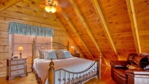 Un dormitorio acogedor con techo de madera, estructura de cama de metal, mesita de noche, cómoda y sofá de cuero.