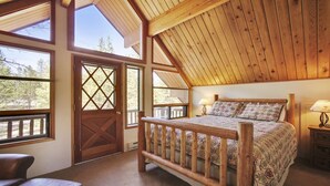 Ein Schlafzimmer mit Holzboden, großen Fenstern, einem Bett mit gemusterten Textilien und einem Nachttisch mit Lampe.