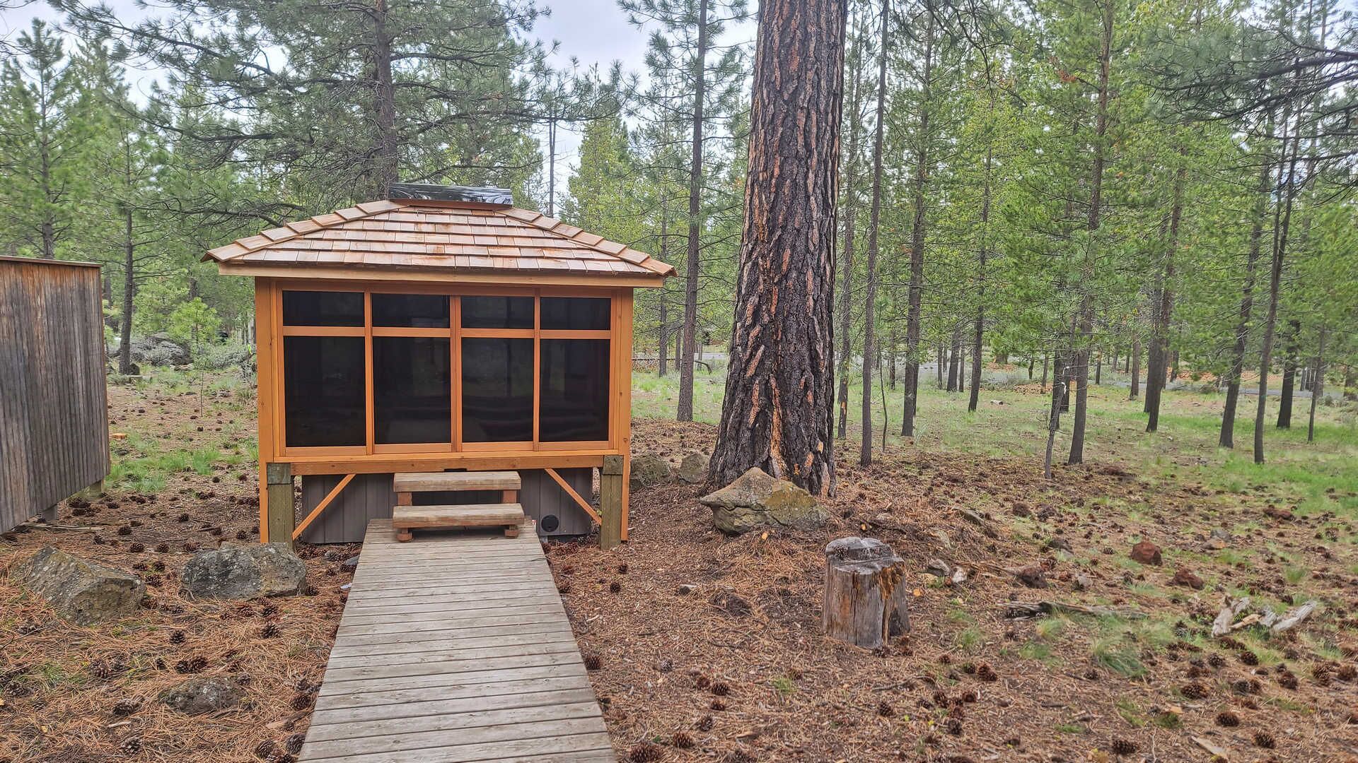 Una petita cabana de fusta amb teulada inclinada i grans finestres, envoltada per un bosc.