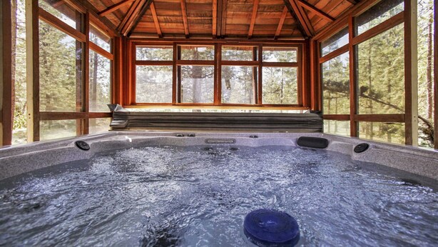 Ein Whirlpool in einer Holzhütte mit großen Fenstern und Blick auf den Wald.