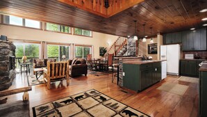 A spacious living area with a stone fireplace, wooden ceiling, and large windows offering a view of the outdoors. - Mountain views, pet friendly, game rooms, 3 king bedrooms, and 2 game rooms! (Sevierville)
