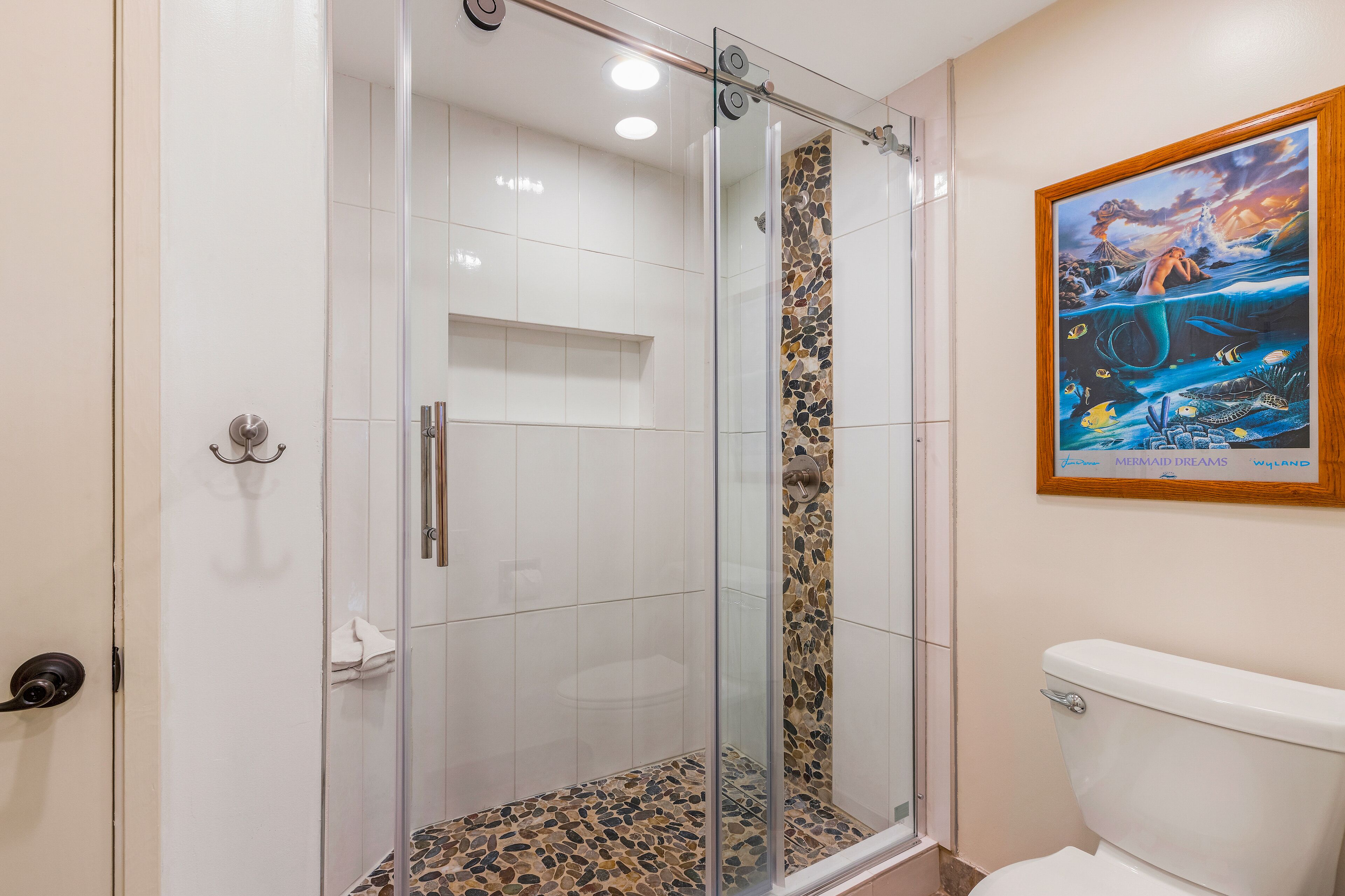 Une salle de bain avec une douche à parois de verre, un carrelage au sol et des toilettes.