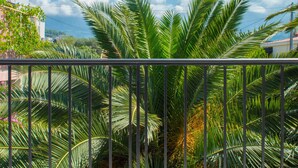 Un balcone con ringhiera metallica, palme e cielo azzurro.