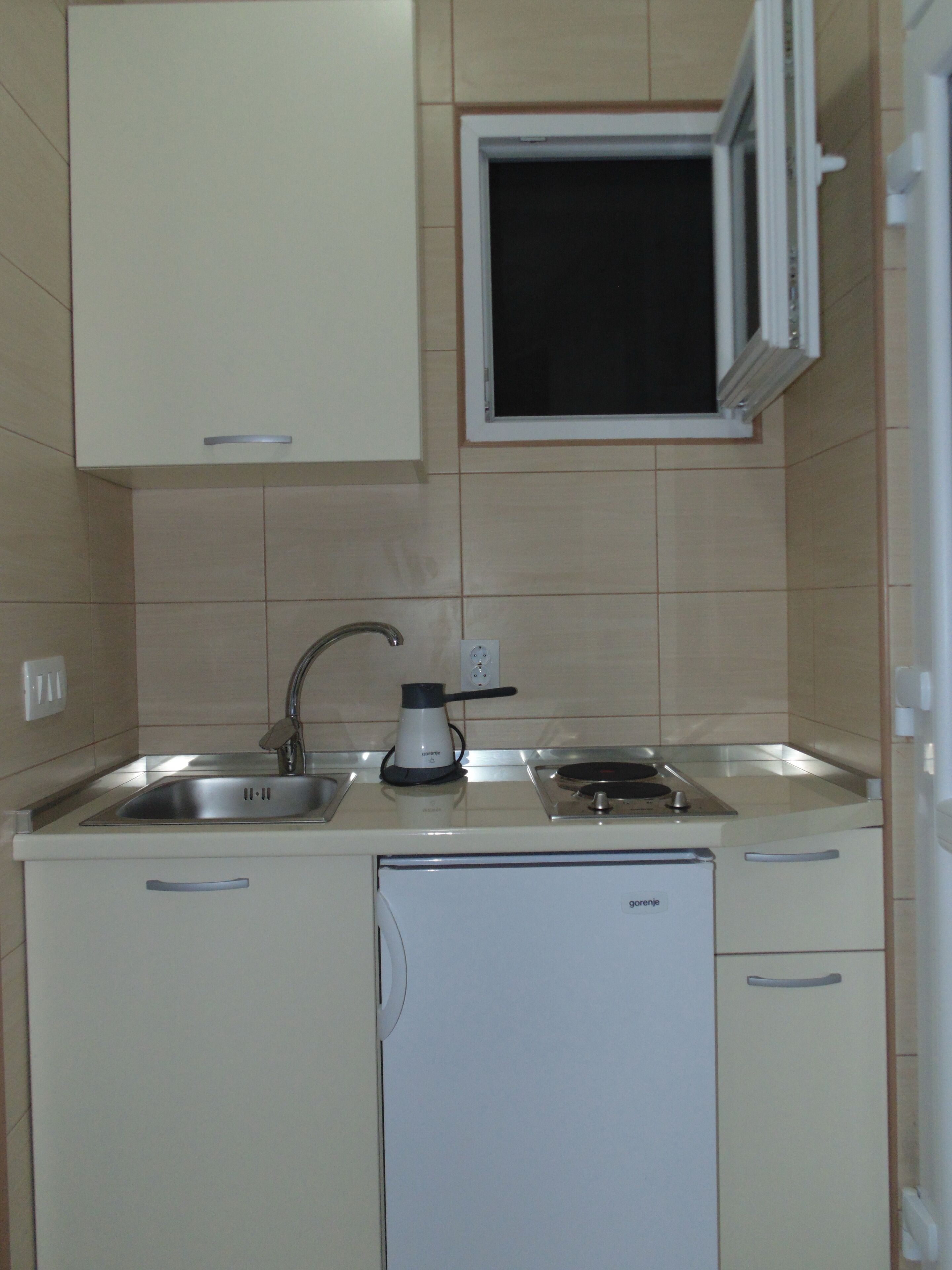 Una cocina compacta con horno integrado, lavamanos y un refrigerador pequeño.