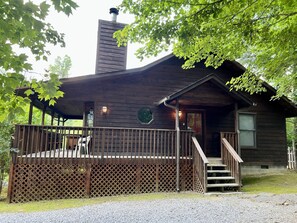 Puuinen mökki, jossa on katettu terassi, savupiippu ja portaat, jotka johtavat sisäänkäynnille.