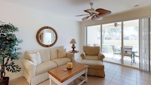 A living room with a sofa, armchair, coffee table, and a large window with a view of the outdoors.