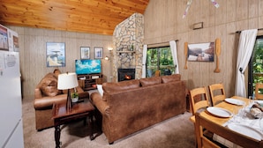 Una sala de estar acogedora con chimenea de piedra, techo de madera y televisor.