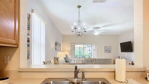 Una cocina con un lavamanos de acero inoxidable doble, una araña, un ventilador de techo y un ventanal con vistas al exterior.