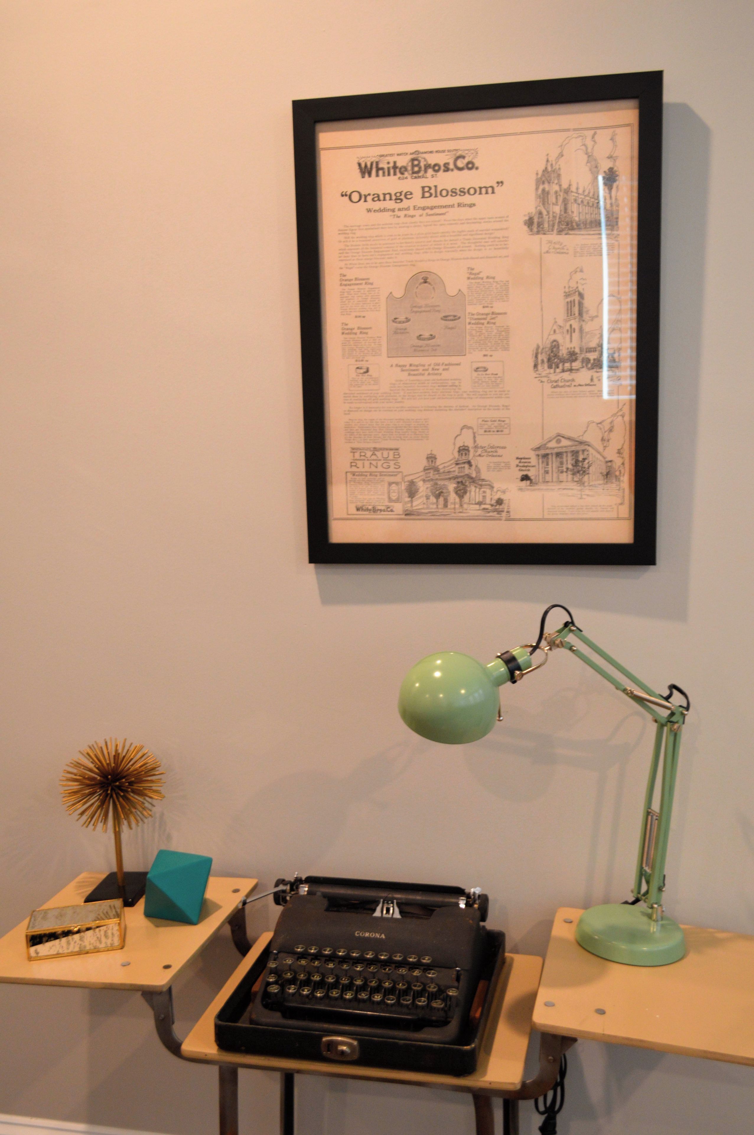 Une vieille publicité encadrée pour la société White Bros. Co., mettant en scène des alliances, une machine à écrire, une lampe et des objets décoratifs sur un bureau.