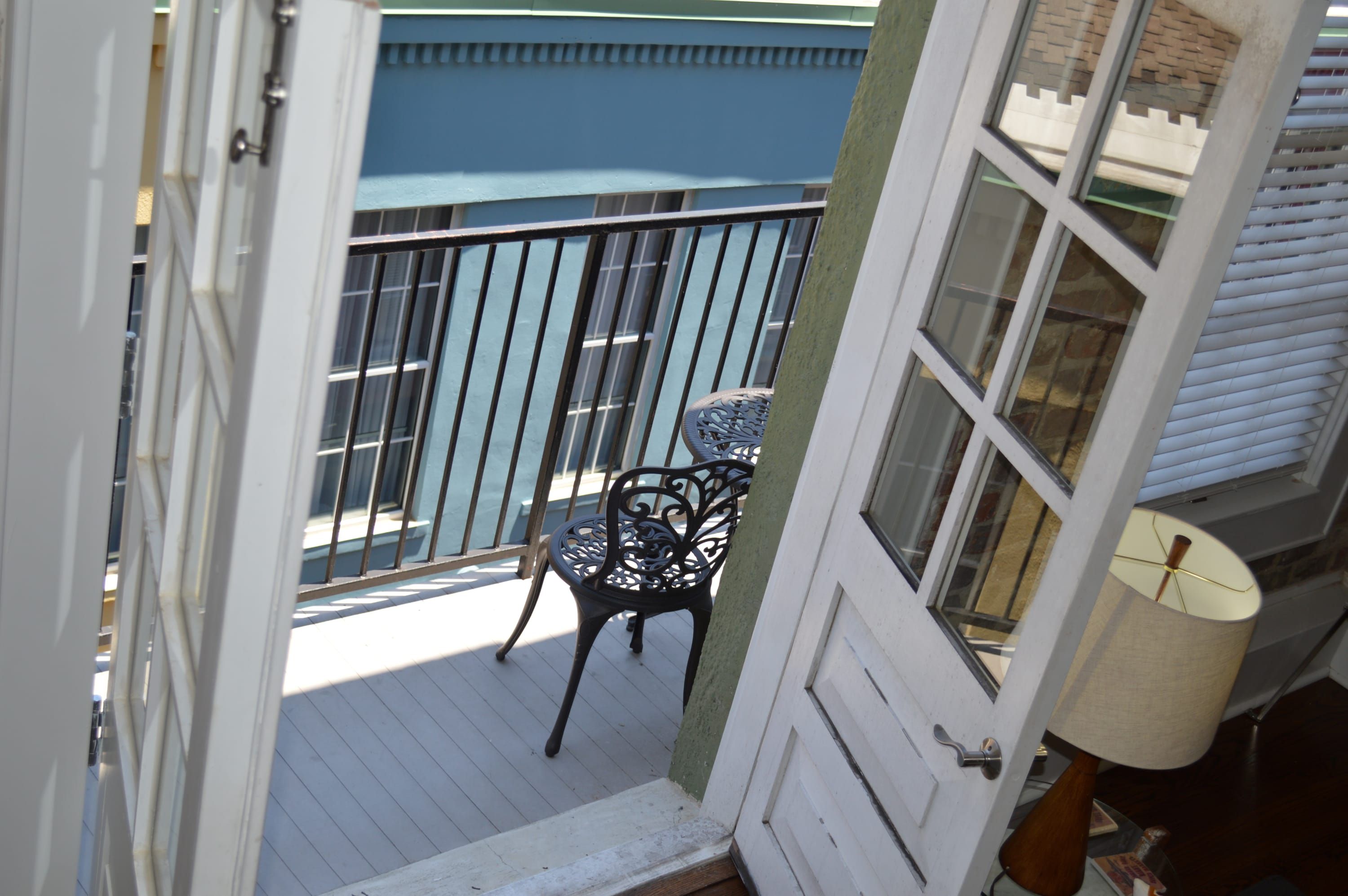 Un balcon avec une chaise et une table, une porte et une fenêtre avec des stores.