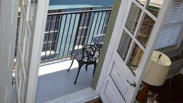 Un balcon avec une chaise et une table, une porte et une fenêtre avec des stores.