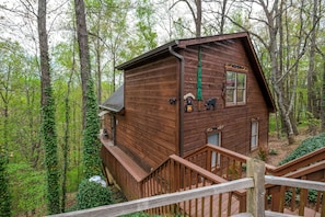 Situated in a forested area, this cabin features a steeply pitched roof and a cozy front entrance with a green door.
