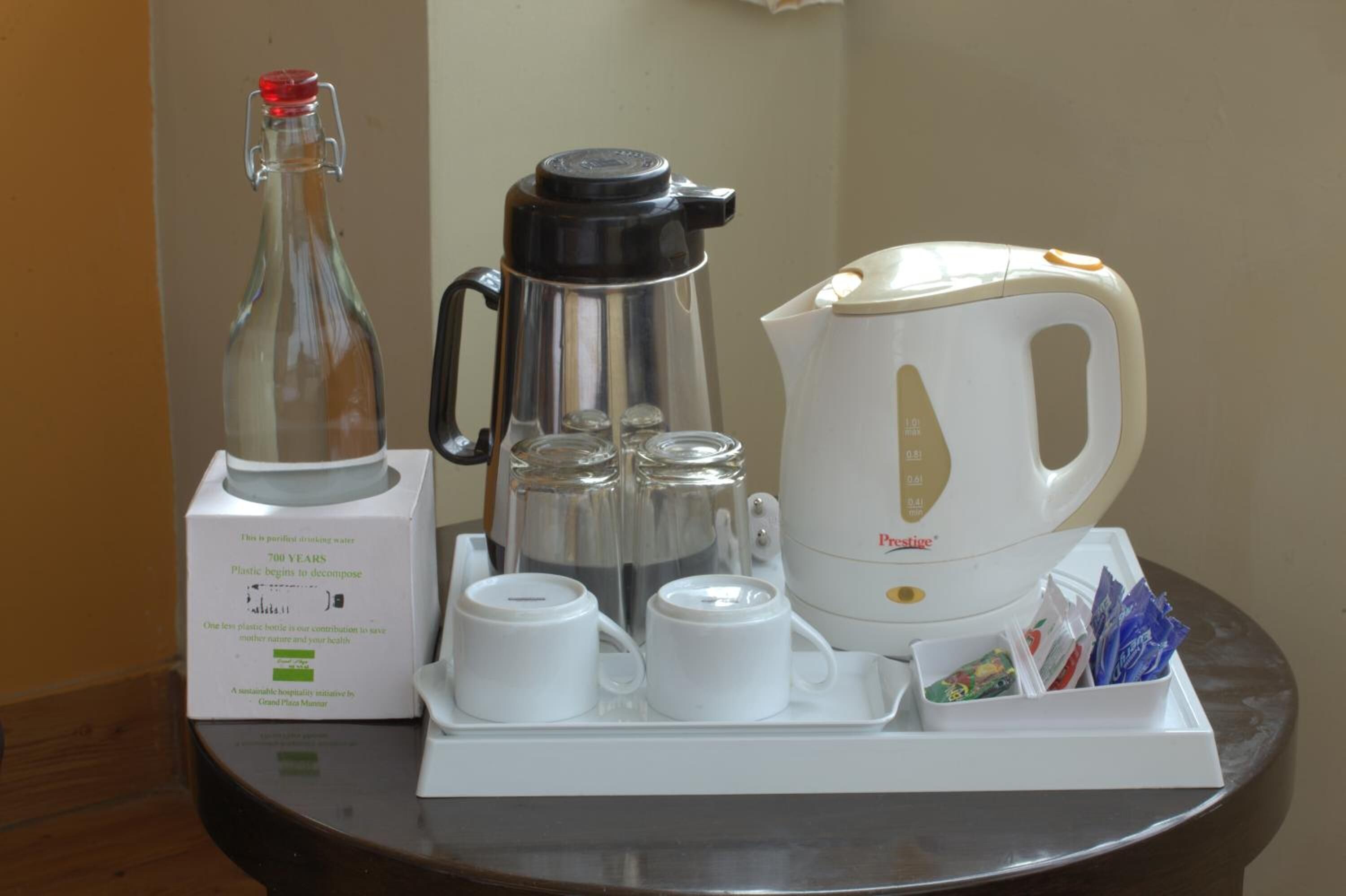 A coffee station with a coffee maker, a bottle of water, a kettle, and a tray with cups and sugar packets.
