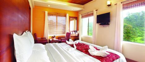 A hotel room with a bed, a desk, a chair, a television, and a window with a view of greenery.