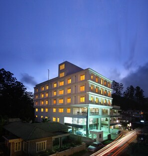 A multi-story hotel with illuminated windows and a modern architectural design. - Grand Plaza Munnar (Devikolam)