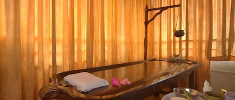 A room with a wooden massage table, a hanging scale, and a set of white containers.