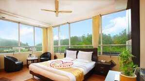 Habitación de hotel moderna con una cama grande, un escritorio, una silla y vistas de la ciudad a través de amplios ventanales.
