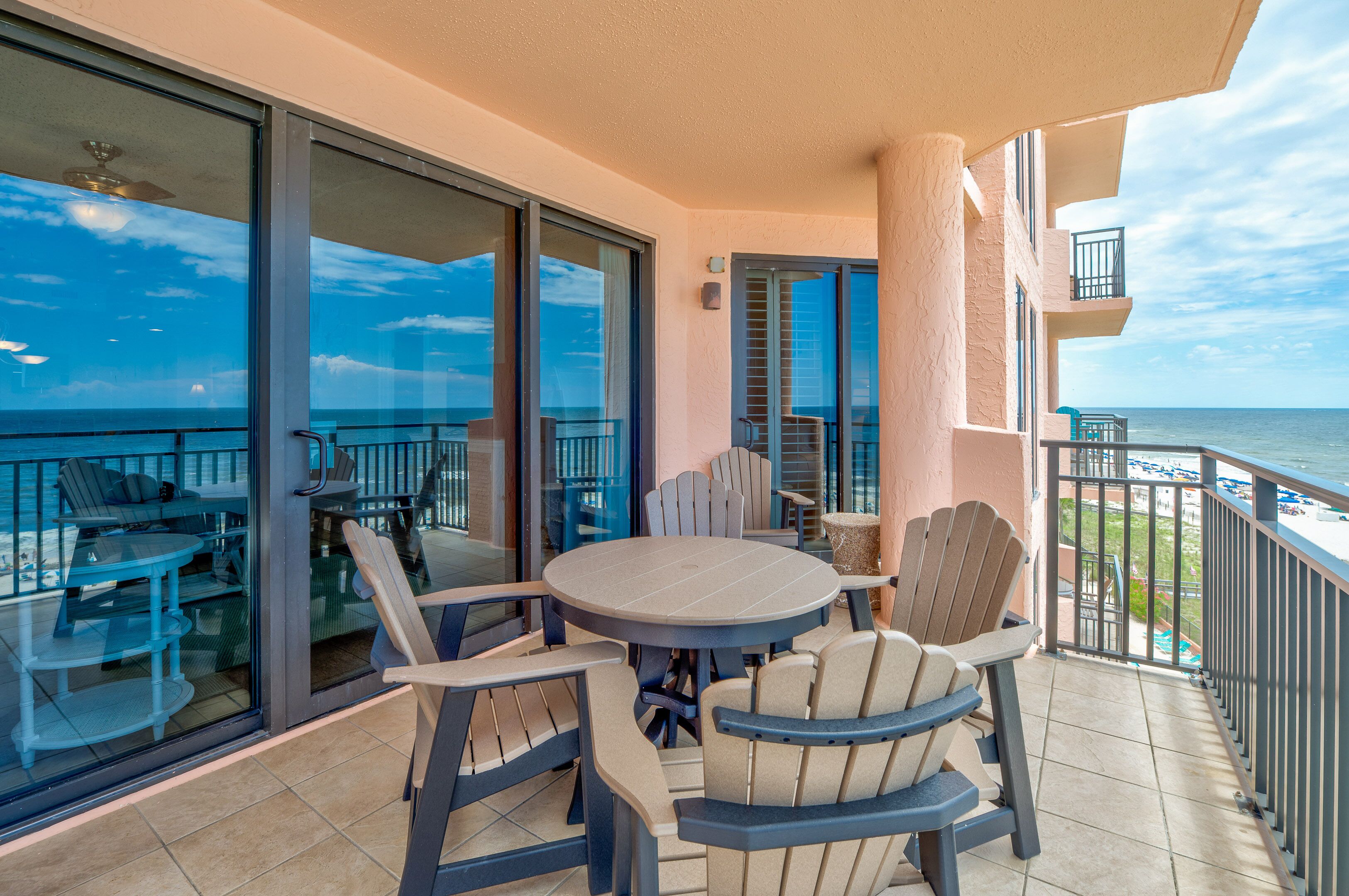 A balcony with a round table and chairs, a glass door leading to a pool area, and a view of the ocean.
