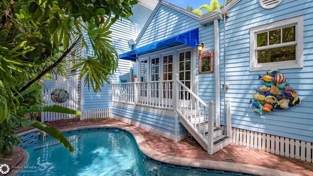 Una casa azul con piscina, barandilla blanca y toldo azul.
