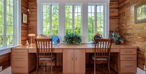 A wooden cabin-style room with a desk, two chairs, and a large window with a view of greenery.