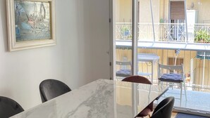 Een eethoek met een marmeren tafel en zwarte stoelen, een schilderij aan de muur, en uitzicht op het balkon met buitenmeubilair.