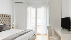 Een moderne hotelkamer met een bed, een bureau met een televisie en een balkon met gordijnen.
