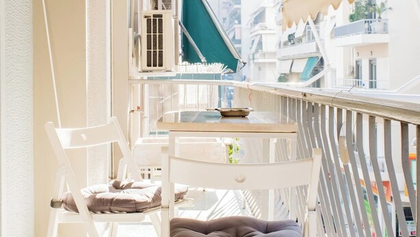 Een balkon met een witte tafel, twee stoelen en een comfortabele bank.
