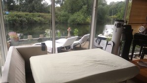 Una habitació amb un llit, una cadira i una taula a prop d'una finestra amb vista a un cos d'aigua.