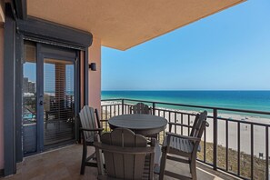 A balcony with a table and chairs, a view of the beach, and a door with blinds.