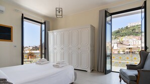 Ein Hotelzimmer mit Bett, Kleiderschrank, Stuhl und einem Balkon mit Blick auf die Stadt.