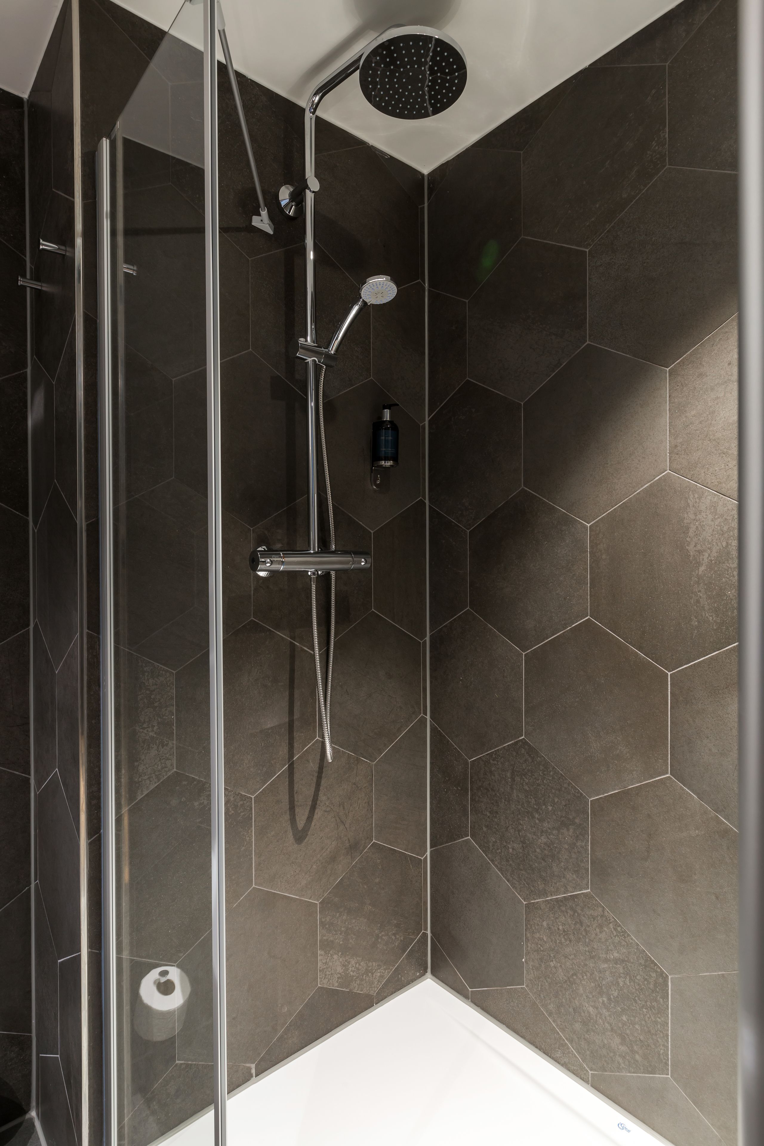 Een douche met een glazen deur, een handdouche en een wandmengkraan.