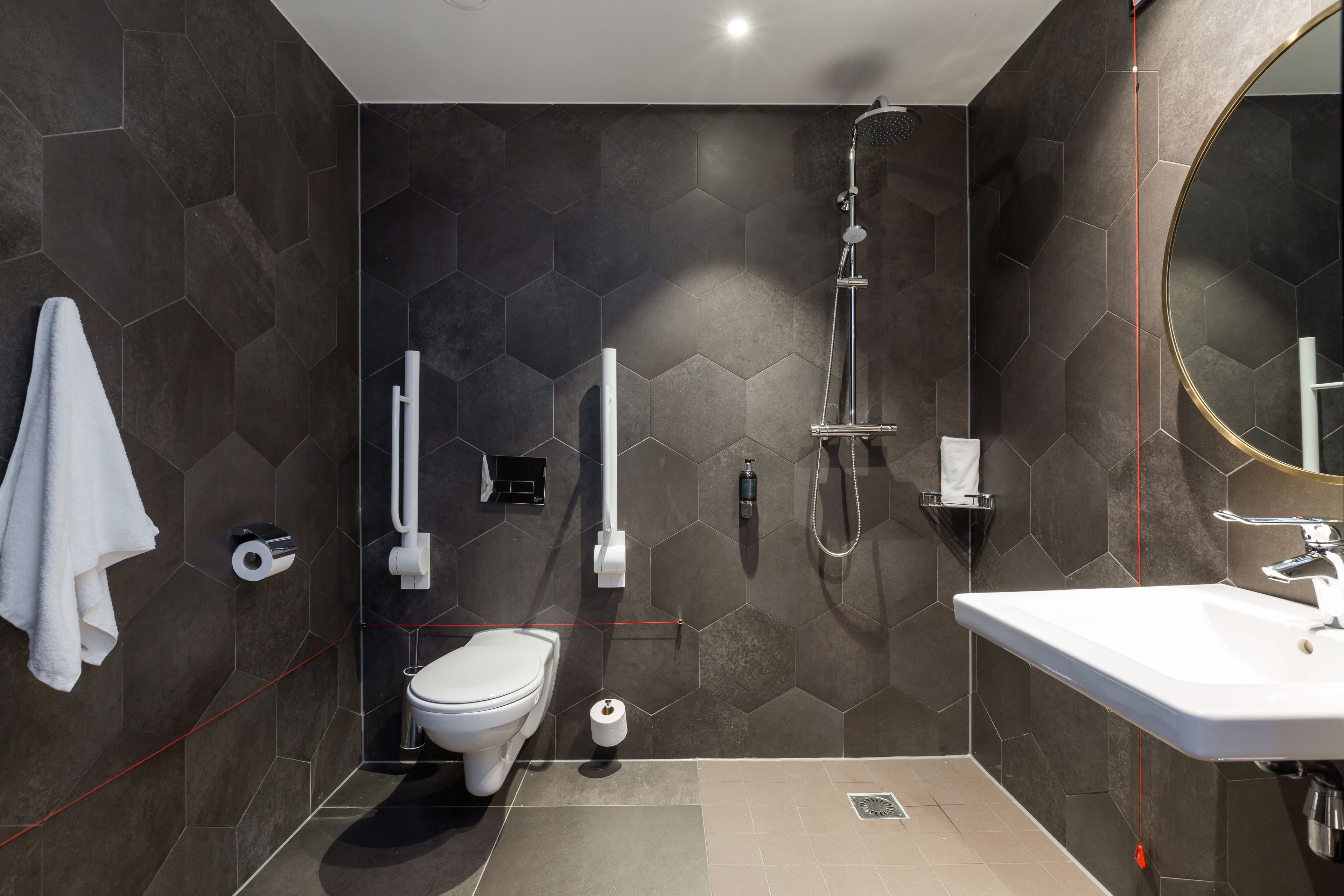 Un baño moderno con pared de azulejos hexagonales, inodoro, lavabo y ducha.