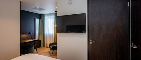 Una habitación de hotel moderna con una cama, un escritorio con una silla, un televisor montado en la pared y una puerta de madera oscura.