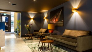 A modern lobby with a sofa, two side tables, a vase with flowers, and wall-mounted lights.