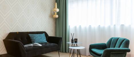 Un salon moderne avec un canapé noir, un fauteuil turquoise et une petite table ronde agrémentée de deux bougies.