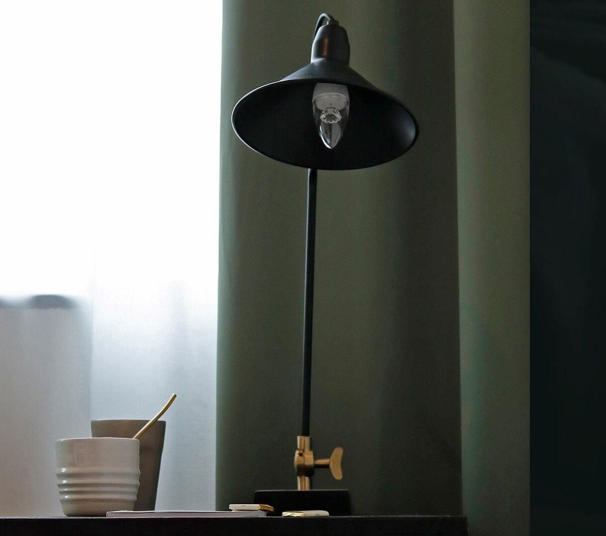 A desk with a black desk lamp, a white cup, and a spoon.