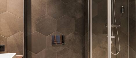 A modern bathroom with hexagonal tiles, a glass-enclosed shower, and a white toilet.
