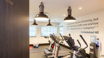 Een fitnessruimte met trainingsapparatuur, een motiverende quote op de muur en een waterdispenser.